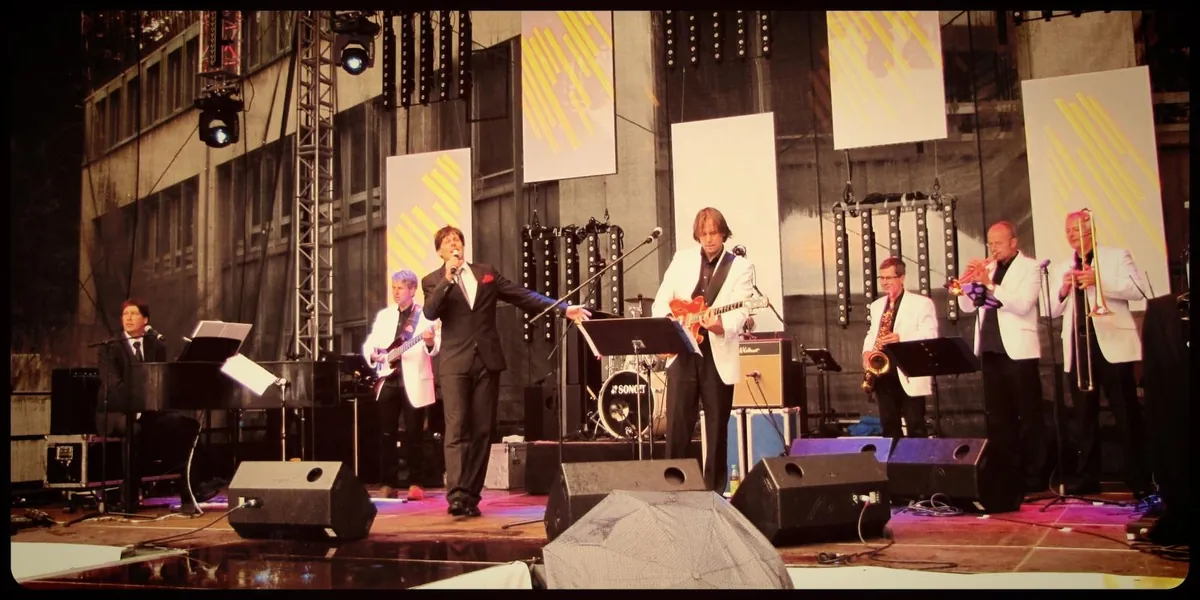 Die Udo-Jürgens-Tribute-Band in weißen Sakkos auf einer großen Open-Air-Bühne mit Lichttraversen